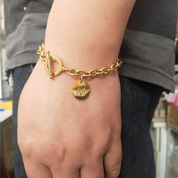 Bracelet initiale en chaines dorées et maillons sur un poignet