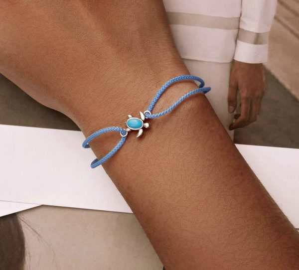 un bracelet bleu en corde avec une tortue en pendentif autour d'un poignet
