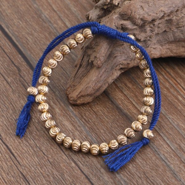 Bracelet bouddhiste tibétain en fil de coton tressé à la main, nœuds porte-bonheur pour femmes et hommes, perles en laiton posé sur un morceau de bois.