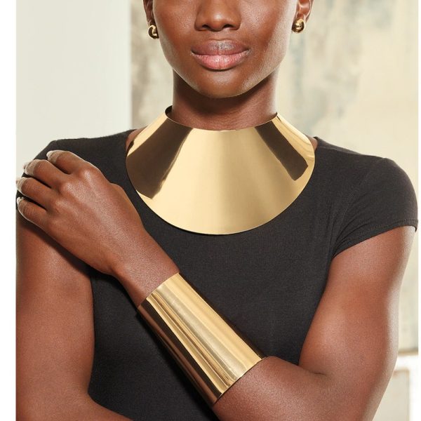Une femme potant une machette dorée au poignet et un collier doré, elle a un tee-shirt noir.