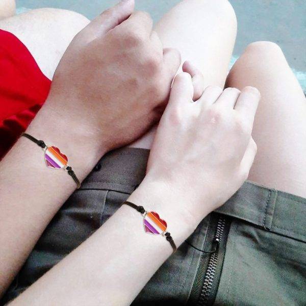 Deux poignets de jeunes filles qui se tiennent le petit doigt avec des bracelets coeur aux poignets.